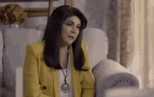 a woman is sitting in a chair wearing a yellow jacket and a necklace .