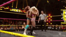 two women are wrestling in a wrestling ring with a referee watching ..