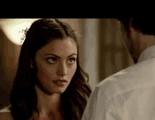 a man and a woman are looking at each other in a room . the woman has a flower in her hair .