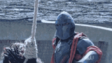 a man in a knight 's outfit is holding a rope with the letter w on his arm