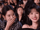 a woman covering her mouth with her hand while another woman looks on