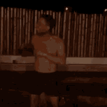 a shirtless man in shorts is dancing in a hot tub at night .