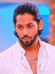 a man with a beard wearing a white shirt and a necklace .