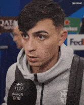 a young man wearing a grey hoodie is holding a microphone that says barca one