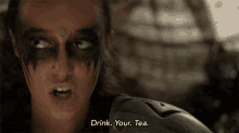 a woman with face paint on her face says drink your tea .