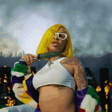 a woman with yellow hair and white glasses is holding a green object in her mouth .
