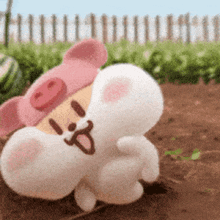 a stuffed animal wearing a pink pig hat is laying in the dirt .