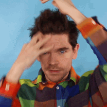 a man wearing a colorful plaid shirt holds his hand to his forehead