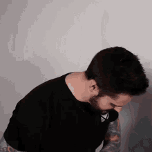a man with a beard and tattoos on his arms is wearing a black t-shirt .