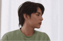a young man in a green shirt is looking at the camera while sitting in front of a window .
