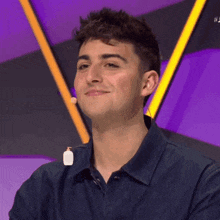 a young man in a blue shirt is smiling in front of a purple background .
