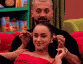 a man and a woman are sitting on a red couch . the woman is wearing a red dress .