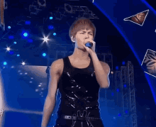 a man in a black tank top singing into a microphone on stage