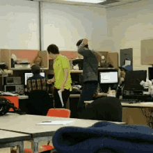 a man in a yellow shirt is standing in a cubicle in front of a computer