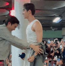 a man in a white tank top is being held by another man in a grey jacket