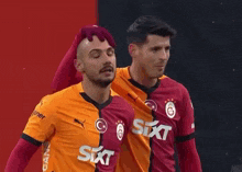two soccer players are standing next to each other and one has a mohawk .