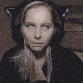 a woman wearing headphones with cat ears on her head makes a funny face