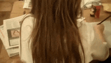 a woman with long hair is sitting at a table with papers and a pencil .