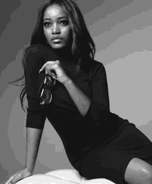 a black and white photo of a woman in a black dress holding a pair of sunglasses