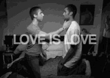 a black and white photo of two men kneeling on a bed with the words `` love is love '' written on the bottom .