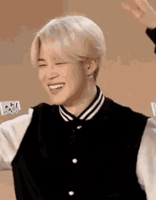 a man with white hair is wearing a black and white baseball jacket and smiling .