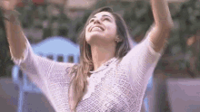 a woman in a white sweater is standing with her arms in the air and smiling .