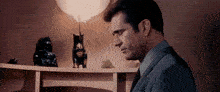 a man in a suit and tie is looking at a cat statue on a bookshelf