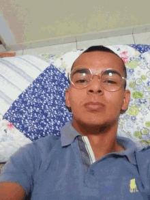 a man wearing glasses is laying on a bed with a blue shirt that says polo