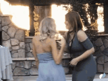 two women are standing next to each other in front of a stone wall holding wine glasses .