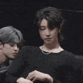 a man wearing a black shirt and a chain around his neck is sitting next to another man