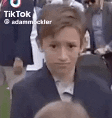 a young boy in a suit is making a funny face while standing in front of a crowd .