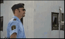 a police officer wearing sunglasses and a hat stands in front of a white building