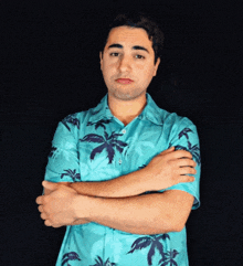 a man wearing a blue shirt with palm trees on it stands with his arms crossed