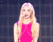 a blonde woman in a pink dress is holding a microphone in her mouth