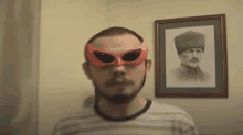 a man wearing a red mask and sunglasses is standing in front of a picture of a man in a hat .