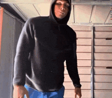 a man in a black hoodie and blue jeans is standing in a garage .