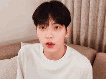 a young man in a white shirt is sitting on a couch with his mouth open