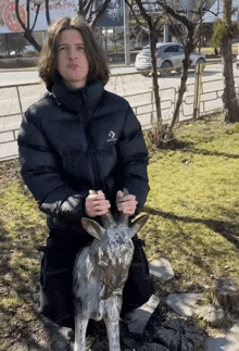 a man in a black converse jacket is kneeling down next to a statue of a goat