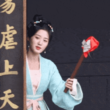a woman in a blue and pink dress holds a red object in front of a sign with chinese writing