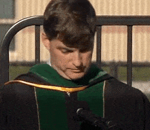 a man wearing a graduation cap and gown is speaking into a microphone