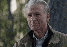 a man with gray hair and a tan jacket looks at the camera