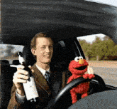 a man in a suit is holding a bottle of wine while elmo sits in the driver 's seat