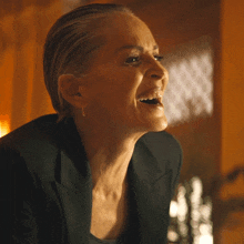 a woman in a black jacket is laughing with her mouth wide open