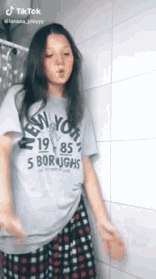 a girl wearing a new york shirt and plaid shorts is dancing in a bathroom .