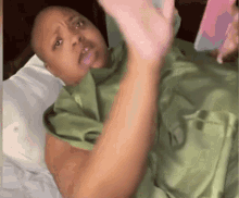 a woman in a green shirt is laying in a bed with a cell phone .