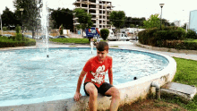 a boy wearing a red shirt with the number 80 on it sits in a fountain