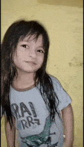 a little girl with long hair is wearing a shirt with a dinosaur on it and looking at the camera .