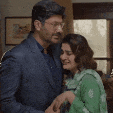 a man in a suit and a woman in a green dress are hugging each other .