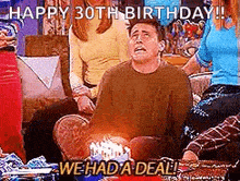 a man is sitting on a couch with a birthday cake in front of him and a group of people .