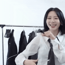 a woman wearing a white shirt and black tie is smiling in front of a rack of clothes .
